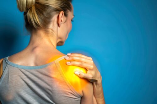 A woman with a sore shoulder is holding her arm to her face. Concept of discomfort and pain